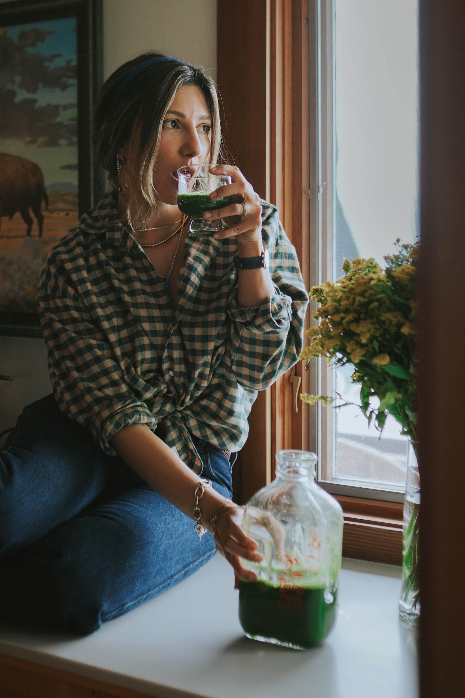 Person sitting by a window with a bottle of Laka Matcha liquid and flowers.